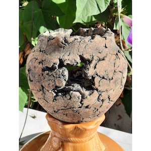 May include: A brown ceramic planter with a crackled finish and a large hole in the side. The planter is sitting on a brown pedestal.