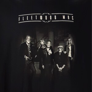 May include: Black t-shirt featuring the band Fleetwood Mac. The band members are depicted in a black and white photograph. The band's name is printed in white, arched across the top of the image.