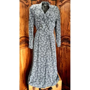 Puede incluir: Un vestido largo de manga larga, largo midi, con un estampado de cachemira en tonos grises y blancos. El vestido presenta un cuello camisero, un corpiño cruzado y una cintura entallada. El vestido se exhibe en un maniquí.