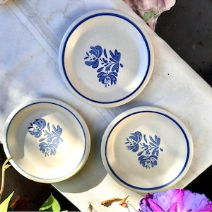 May include: Three white ceramic plates with blue floral designs. The plates have a simple, rustic look and are perfect for everyday use.