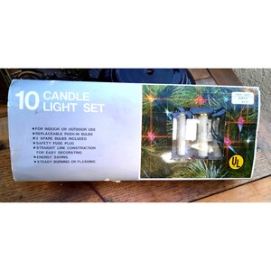 May include: A box of 10 white candle light bulbs with a green pine tree background. The box says "10 Candle Light Set" and lists features like "For Indoor or Outdoor Use", "Replaceable Push-In Bulbs", "#2 Spare Bulbs Included", "Safety Fuse Plug", "Straight Line Construction", "For Easy Decorating", "Energy Saving", "Steady Burning or Flashing".