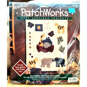 Pode incluir: Um kit de projeto de aplicação fácil Bucilla PatchWorks. O kit inclui patches de tecido com desenhos de animais, incluindo uma girafa, uma zebra, um elefante e um sapo. O kit também inclui o texto "Two by Two" e "Patches apply quickly with fusible web!"