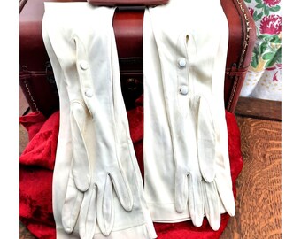 May include: A pair of long white gloves with white buttons. The gloves are laying on a red surface.