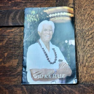 May include: A black and white photo of a man wearing a white shirt and a lei. The text "Prince Kuhio" is at the top of the image. The text "Nou Ka Hale" is at the bottom of the image.