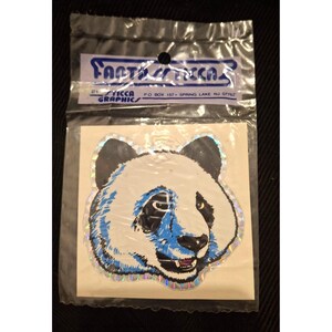 May include: A panda sticker in a clear plastic package. The panda has a white face with black ears and eyes, and blue accents. The sticker is from "STICCA GRAPHICS" and the package has the text "FANTASTICCA".