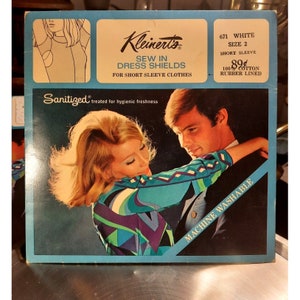 Puede incluir: Un paquete vintage de protectores de vestido Kleinert's para coser, con una pareja en un abrazo romántico. El paquete es azul y blanco con el texto "Sanitized tratado para una frescura higiénica" y "Lavable a máquina".