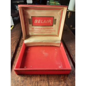 May include: Red velvet watch box with gold trim. The lid is open and shows a white label with the text "BELAIR 25 JEWELS-AUTOMATIC SHOCK RESISTANT ANTI-MAGNETIC UNBREAKABLE MAINSPRING".
