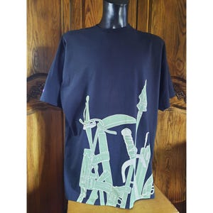May include: A navy blue t-shirt featuring a white graphic print of various weapons, including a sword, a sickle, and a spear.