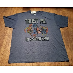 May include: A blue t-shirt with a graphic of Captain America, Iron Man, and Thor. The text on the shirt reads "Trust Me I'm A Super Hero."