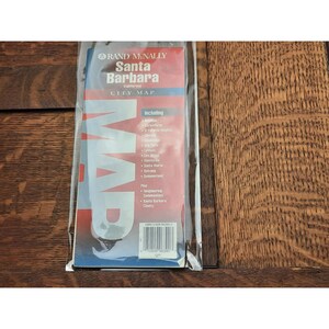 May include: A red and white Rand McNally city map of Santa Barbara, California. The map includes surrounding communities and Santa Barbara County. The map is in a plastic sleeve.