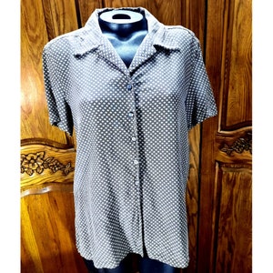 Puede incluir: Una camisa de botones gris y blanca con estampado, de manga corta. La camisa tiene cuello y cierre de botones.