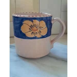 May include: A ceramic mug with a blue and white floral design. The mug has a pink rim and a handle.