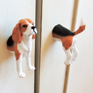 May include: Two white cabinet door knobs shaped like a beagle dog. One knob features the dog's head and the other knob features the dog's rear end.