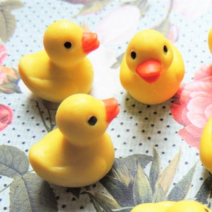 May include: Seven yellow rubber duck toys on a floral background. The ducks are all facing different directions and have black eyes and orange beaks.