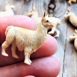 May include: A collection of small, tan-colored llama figurines. The figurines are detailed with textured fur and stand on four legs. Some llamas are in focus, while others are blurred in the background, creating a sense of depth.