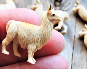 Op de afbeelding: Een verzameling kleine, beige lama-beeldjes. De beeldjes zijn gedetailleerd met getextureerde vacht en staan op vier poten. Sommige lama's zijn scherp, terwijl andere op de achtergrond wazig zijn, wat een gevoel van diepte creëert.