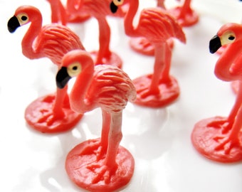 May include: A group of pink plastic flamingo figurines on a white surface. The flamingos are all facing the same direction and have black eyes and beaks.