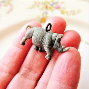 May include: A gray rhinoceros charm with a bronze loop for hanging. The charm is detailed with textured skin and a curled horn.