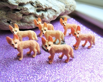 May include: A set of six small, orange-brown plastic figurines of foxes. The foxes are standing on a purple sparkly surface.