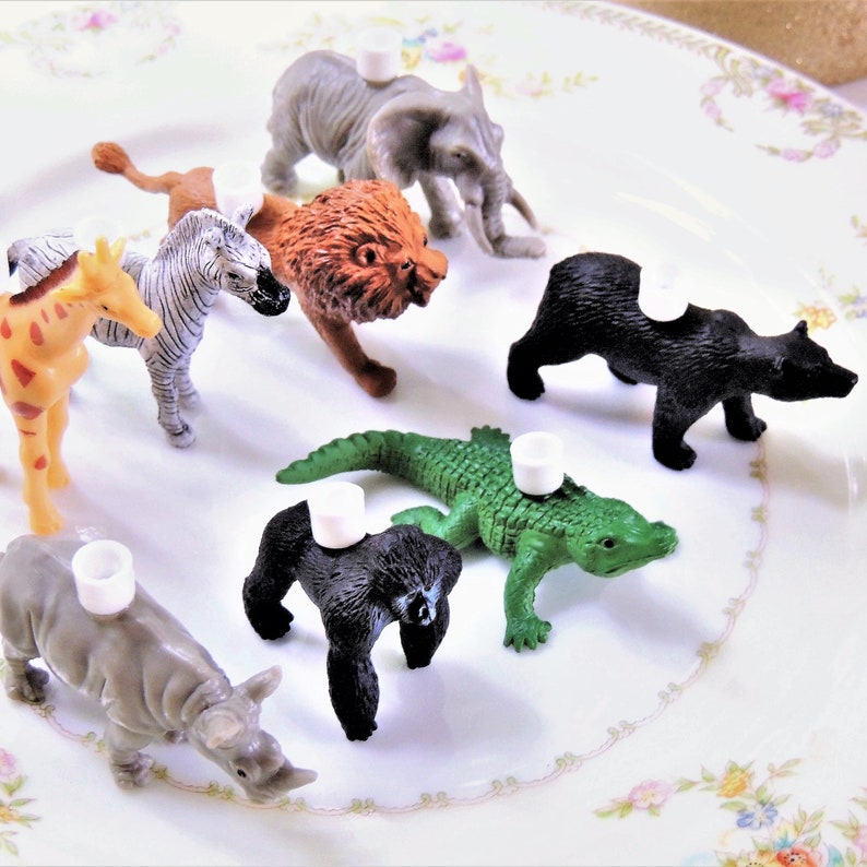 May include: A set of nine plastic animal figurines, including a giraffe, zebra, lion, elephant, bear, alligator, gorilla, and rhinoceros. Each figurine has a white plastic disc on top.