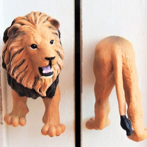 May include: A lion figurine with a black mane and brown fur. The figurine is standing on its hind legs with its head facing forward and its mouth open. The figurine is a decorative door knob.