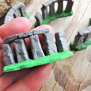 May include: A miniature stonehenge model with gray stones and green grass. The model is made of plastic and is about 5 inches long.