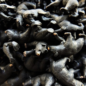May include: A pile of black plastic toy bears, all in various poses, with some bears stacked on top of others.
