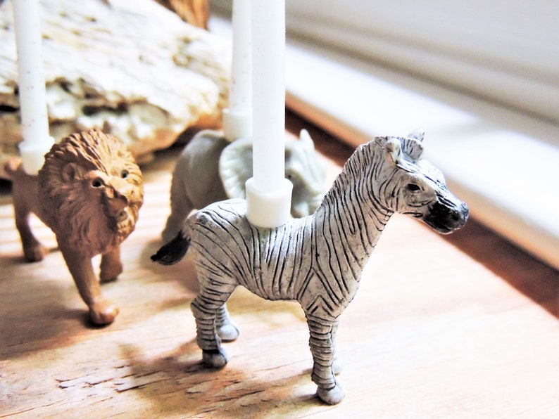 May include: A set of animal candle holders featuring a zebra, a lion, and a rhinoceros. The candle holders are made of a white ceramic material and are designed to hold small candles.