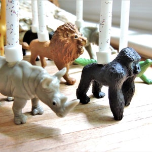 May include: A set of animal figurines with white candles, perfect for a birthday cake. The figurines include a zebra, giraffe, lion, rhinoceros, gorilla, and a green alligator.