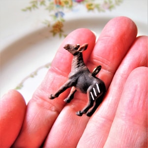 May include: A small, brown and white figurine of an okapi, a type of mammal native to the Democratic Republic of the Congo. The figurine is made of plastic and has a loop on the top for hanging.