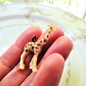 May include: A small plastic giraffe charm with brown spots, a light brown body, and a black metal loop for hanging.