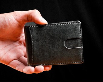 May include: A black leather wallet being held in a hand, with a black background.