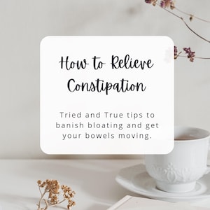 May include: A white card with the text "How to Relieve Constipation" and "Tried and True tips to banish bloating and get your bowels moving."  The card is on a white surface with a white teacup and saucer and dried flowers.