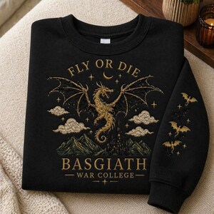 Puede incluir: Sudadera negra con un dise&ntilde;o de drag&oacute;n dorado, las palabras "FLY OR DIE" y "BASGIATH - WAR COLLEGE" est&aacute;n impresas en la parte delantera. La manga tiene un dise&ntilde;o de dragones dorados. El dise&ntilde;o incluye nubes, estrellas y una luna creciente.