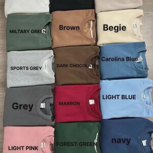 Puede incluir: Una cuadr&iacute;cula de sudaderas plegadas en varios colores, cada una etiquetada con su nombre de color. Los colores incluyen blanco, negro, arena, verde militar, marr&oacute;n, beige, gris deportivo, chocolate oscuro, azul Carolina, gris, granate, azul claro, rosa claro, verde bosque y azul marino.