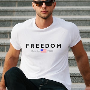 May include: White t-shirt featuring the word "FREEDOM" in black capital letters. Underneath, the text reads "Charlie Kirk", an American flag graphic, and the dates "1993-2025".