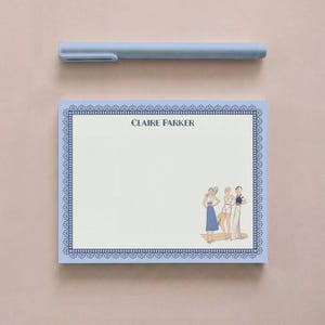 May include: A light blue notepad with a dark blue decorative border and the name CLAIRE PARKER printed at the top. The bottom right corner features an illustration of three figures in vintage attire. A light blue pen rests above the notepad.