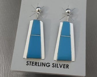 May include: A pair of sterling silver earrings with blue turquoise stones. The earrings are rectangular in shape and have a simple design.