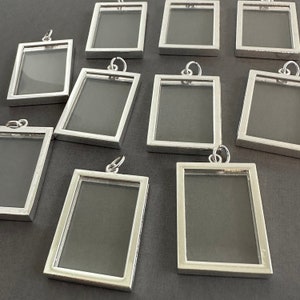 May include: Ten silver-toned picture frames with clear glass inserts. The frames are rectangular and have a simple design. They are all hanging from a small loop at the top.