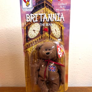 May include: A brown plush bear toy named "Britannia" with a Union Jack flag on its chest, packaged on a card featuring Big Ben. The card also has the text "Collect All 4!" and the Ty logo.