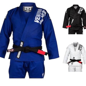 Puede incluir: Tres uniformes de artes marciales en azul, negro y blanco. Cada uniforme tiene un cinturón negro con una raya roja y el logotipo de Venum con caracteres japoneses.