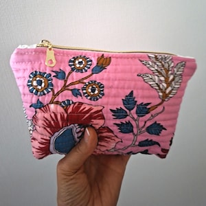 Könnte beinhalten: Ein gestepptes Stofftäschchen mit einem leuchtend rosa Hintergrund und einem Blumenmuster in Blau-, Weiß- und Brauntönen. Das Täschchen verfügt über einen goldfarbenen Metallreißverschluss an der Oberkante und horizontale Steppnähte.
