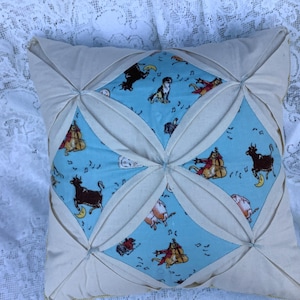 Könnte beinhalten: Quadratisches Zierkissen mit einem hellblauen Mittelteil mit einem skurrilen Muster von Musik spielenden Tieren. Das Kissen hat ein cremefarbenes, gestepptes Design und ein weiches, einladendes Aussehen.