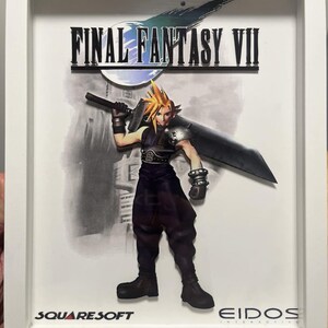 May include: A framed image of a video game character, Cloud Strife, from Final Fantasy VII. He is holding a large sword and is standing in front of a city skyline. The image is surrounded by a white frame and includes the game title "FINAL FANTASY VII", the game developer "SQUARE SOFT", and the publisher "EIDOS INTERACTIVE".