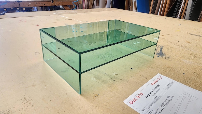 May include: A two-tiered glass coffee table with a clear green tint. The table is made of thick glass and has a modern design.