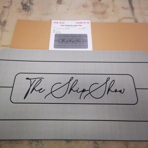 May include: Gray non-slip mat with black lines and the text "The Ship Show" in a cursive font.