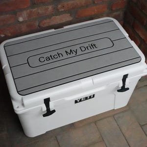May include: White Yeti cooler with a gray, textured lid. The lid has the text "Catch My Drift" printed on it.