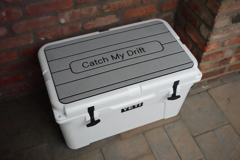 May include: White Yeti cooler with a gray, textured lid. The lid has the text "Catch My Drift" printed on it.