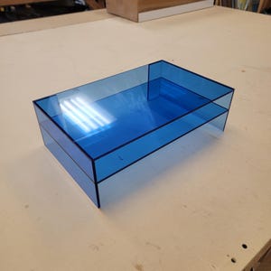 May include: A blue acrylic desktop organiser with two tiers. The organiser is made of clear acrylic and has a light blue tint.