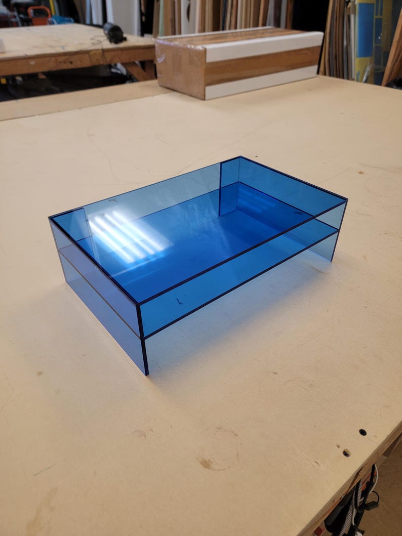 May include: A blue acrylic desktop organiser with two tiers. The organiser is made of clear acrylic and has a light blue tint.